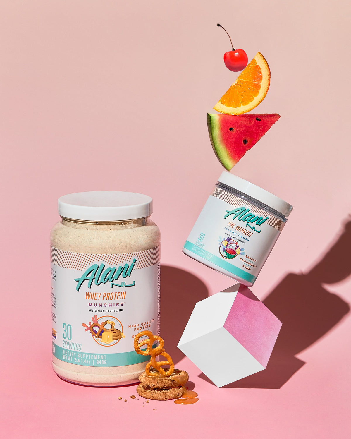A container of Pre-Workout in Island Crush flavor next to Whey Protein in Munchies flavor and pretzels on the side.